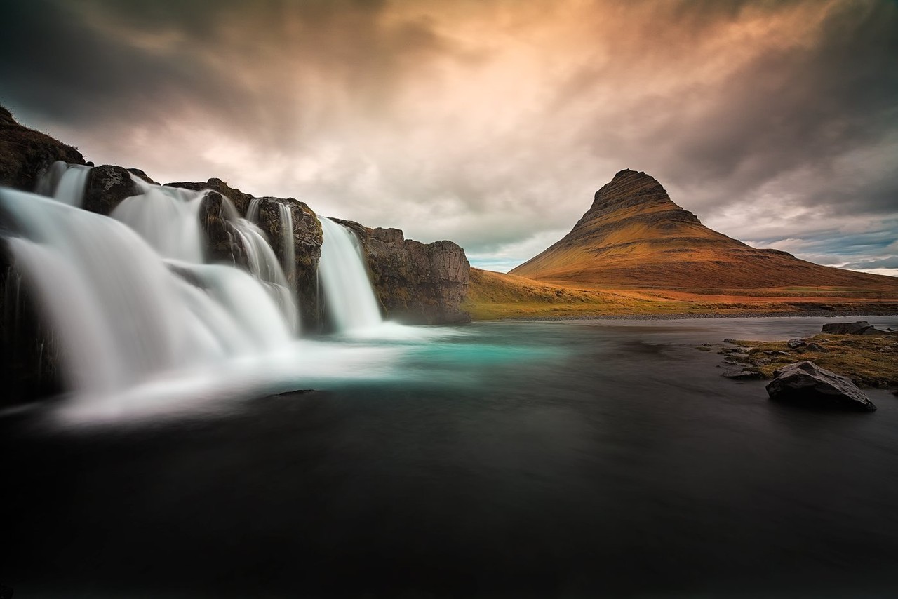 The Kirkjufellsfoss waterfall flows below its mountain under a glowing autumn sky.