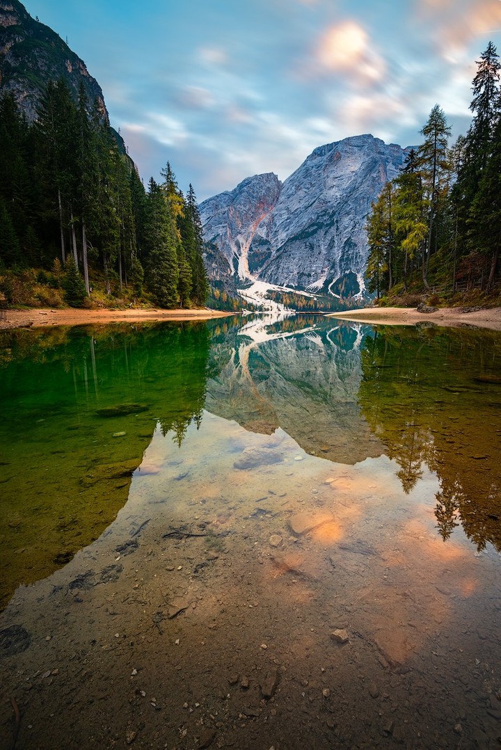 A mountain and evergreen forest reflect in the still water of Lake Braies.