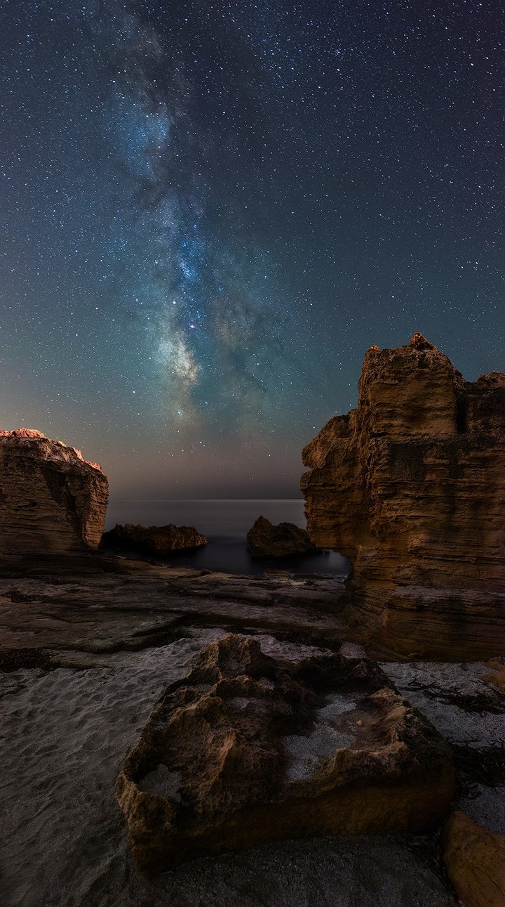 The Milky Way arches over a quiet stretch of Sardinian coast.