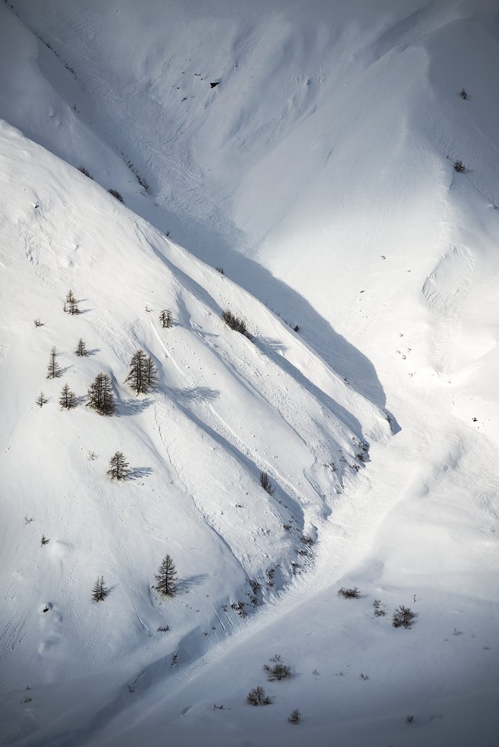 Scattered larch trees mark a steep, snow-covered mountainside.